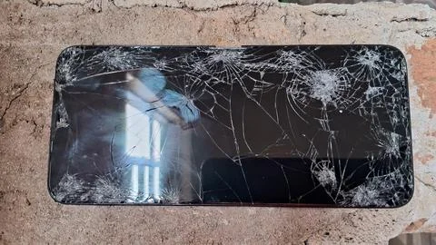 Broken smartphone screen with spiderweb cracks resting on textured concrete Stock Photos