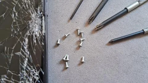 Broken smartphone screen with tiny metal screws and precision repair tools Stock Photos