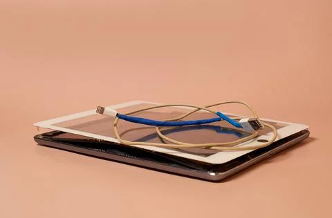 A broken tablet with a swollen battery and a dirty screen and a bare USB wire Stock Photos