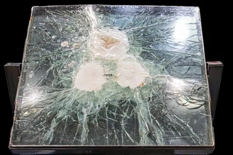 Broken triplex glass table with bullet marks, scattered pieces, metal legs, o Stockfoto's