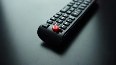 Broken TV remote with loose power button and damaged casing on dark tabletop Stock Footage 331488524