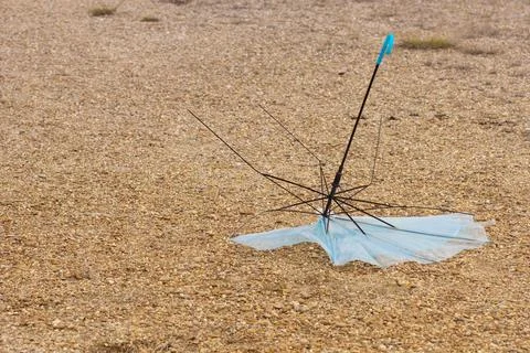 Broken umbrella destroyed by wind lying on sand Stock Photos
