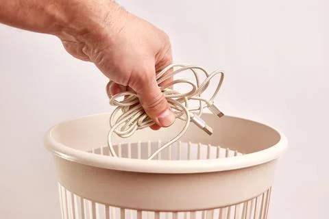 A broken USB cable is thrown into the trash. Disposal and recycling of waste. Stock Photos