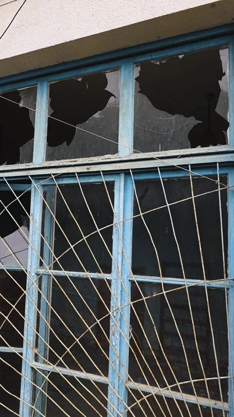 Broken window glass on an abandoned building facade with a weathered blue frame  Vídeo Stock 330436147