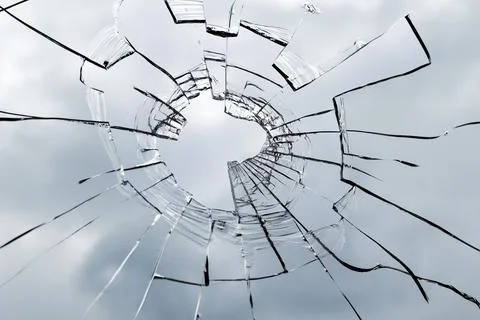 Broken window glass on a background of cloudy sky. Close up. Stock Photos