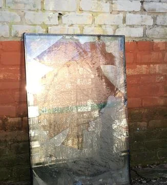 A broken window glass block is shown leaning against a brick wall, in which.. Stock Photos