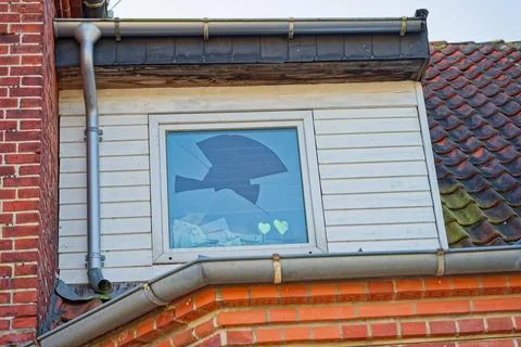Broken window on upper floor of brick and tiled roof house with gutter system Stock Photos