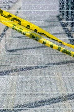 Broken wired mesh glass panel with diagonal yellow caution tape. Foto stock