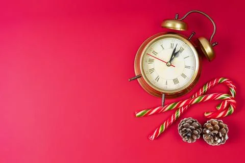 Bronze alarm clock, candy cane and fir cones on red background. Christmas a.. Stock Photos