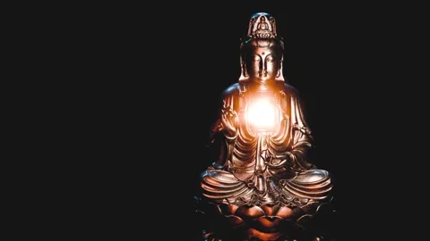 Bronze buddha statue holding a glowing orb, meditating in dark background Stock Footage 305753232