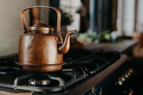 Bronze kettle in modern kitchen. Old vintage teapot on gas stove. Preparing tea Stock Photos