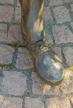 Bronze statue boot stepping on cobblestone pavement with laces and wear mar.. Foto stock