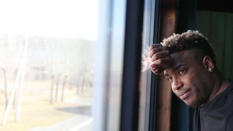 A brooding African guy in a black T-shirt is standing by the window. Stock Footage 220354828