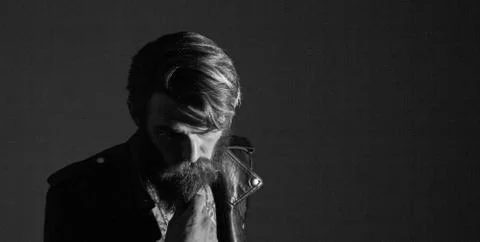 Brooding bearded hipster in a leather jacket looking somewhere t Stock Photos