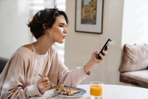 Brooding beautiful girl using mobile phone while having breakfast Stock Photos
