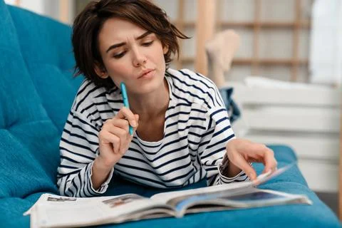 Brooding beautiful student girl doing homework while lying on couch Stock Photos