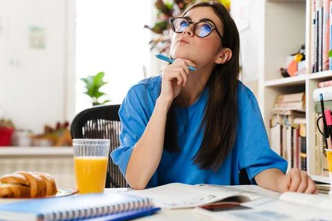Brooding brunette girl doing homework while sitting at table Fotos de archivo