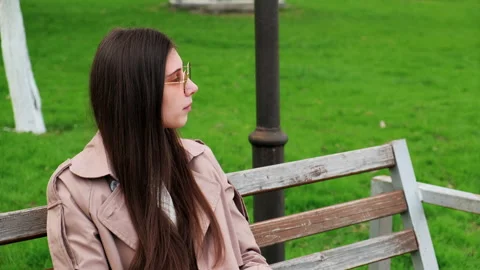 A brooding brunette lady sits at a park. Young girl in coat thought about Stock Footage 152111902