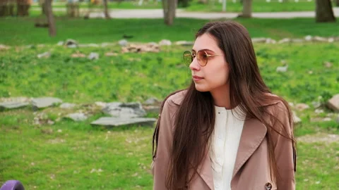A brooding brunette lady sits at a park. Young girl in coat thought about Stock-Footage 152112398