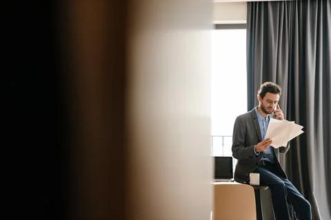 Brooding businessman talking on mobile phone while examining documents Stock Photos