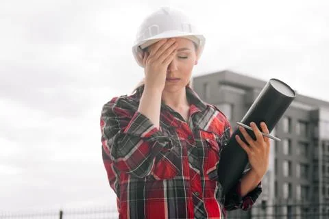 A brooding female builder with drawings of papers in her hands. Stock Photos