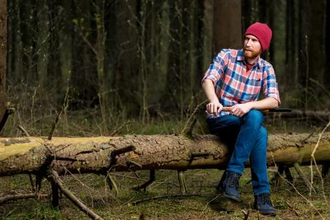 A brooding forester with a beard resting on a fallen tree in the forest Stock Photos