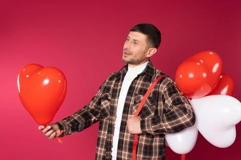 A brooding guy with a bunch of balloons on a red background looks to the side Stock Photos