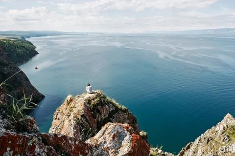 Brooding man sits on the edge of rock in front of the open water space Stock Photos
