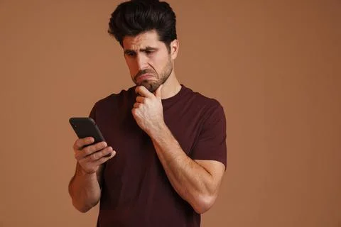 Brooding masculine man using mobile phone while posing on camera Stock Photos