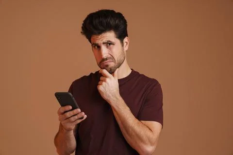 Brooding masculine man using mobile phone while posing on camera Stock Photos