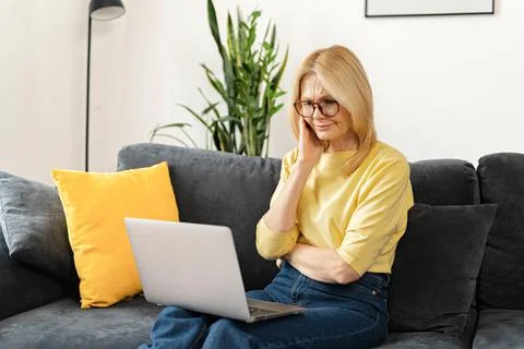 Brooding middle-aged woman using a laptop for remote work at home, studying Stock Photos