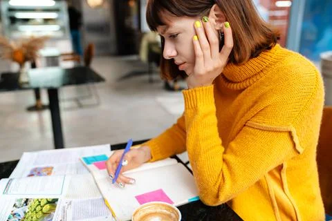Brooding redhead student girl drinking coffee and doing homework Stock Photos