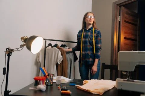 A brooding seamstress stands next to things. Tailor removes clothes on dress  Stock Photos