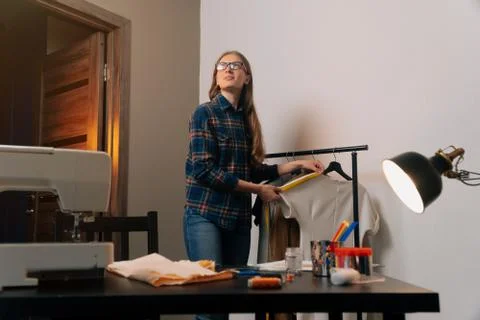 A brooding seamstress stands next to things. Tailor removes clothes on dress  Stock Photos