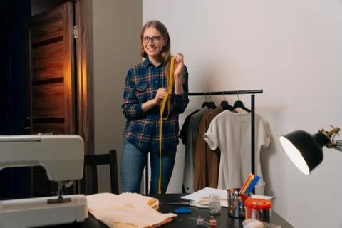 A brooding seamstress stands next to things. Tailor removes clothes on dress  Stock Photos