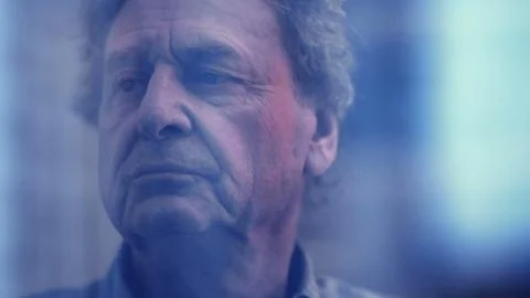 Brooding senior man lost in thought, gazing through his window as the world.. Stock Photos
