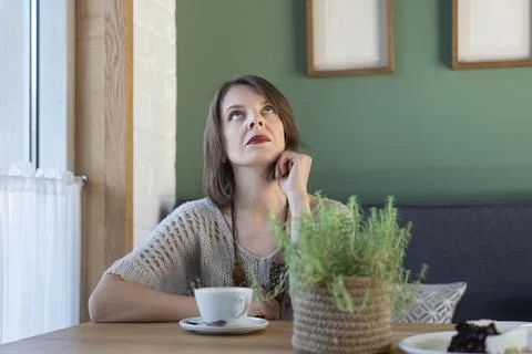 Brooding young woman sits at table in cafe and looks up. Middle-aged woman dr Stock Photos