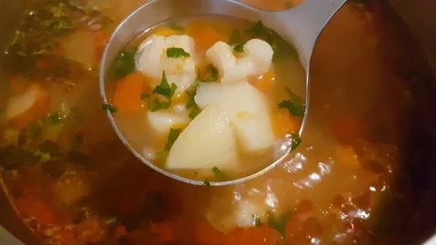 Broth boiling. Using a stainless ladle to take some of it. Vegatables boiling Stock Footage 92525910