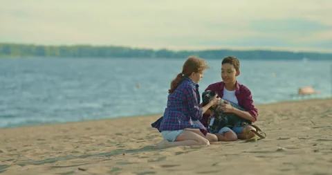 Brother and sister are sitting on the sand by the sea and playing with the dog Stock-Footage 201946292