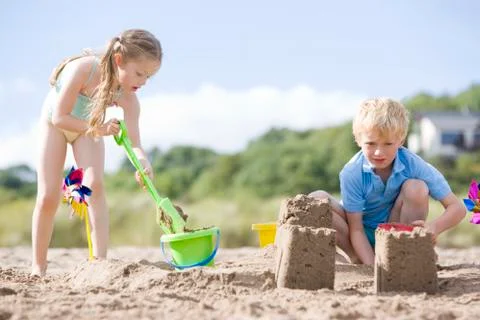 Brother and sister at beach making sand castles Stock Photos