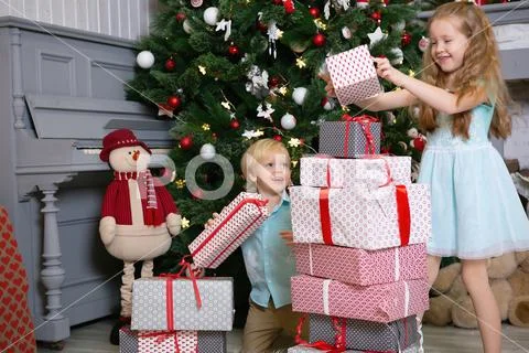 Brother and sister at the christmas tree make a mountain of gifts Stock Photos