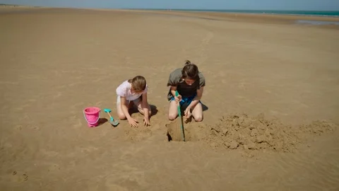 Brother and sister digging big hole in sand with shovel and hands, laughing Stock Footage 329068507