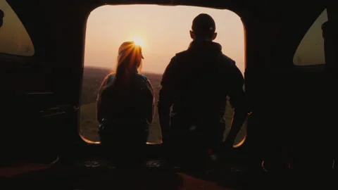 Brother and sister sit side by side in the trunk of the car, watching the sunset Stock Footage 144043785