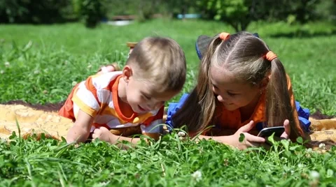 Brother and sister using tablet PC and smartphone lying on the grass 스톡 동영상 56542715