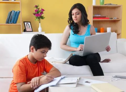 Brother doing homework while his sister using laptop Stock Photos
