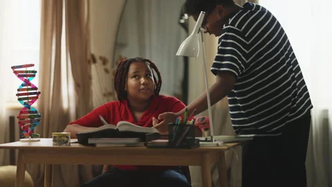 Brother teasing his younger sister for being diligent and doing homework Stock Footage 337092268