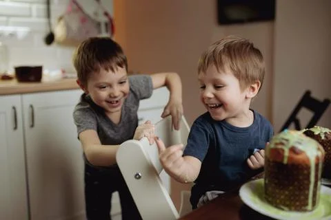 Brothers decorating Easter cakes with glace icing eating sugar topping. Image Stockfoto's