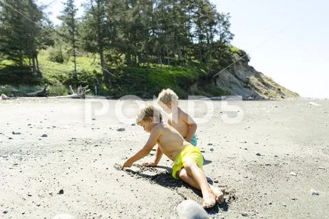 Brothers drawing on sand at beach against clear sky during sunny day Stock Photos