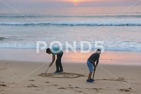Brothers drawing in sand at sunset Stock Photos