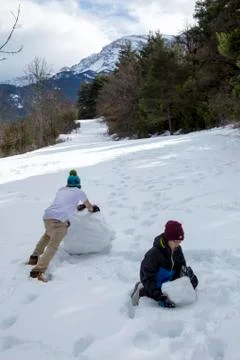 Brothers make a snowman in a winter forest in the mountains. Stock Photos
